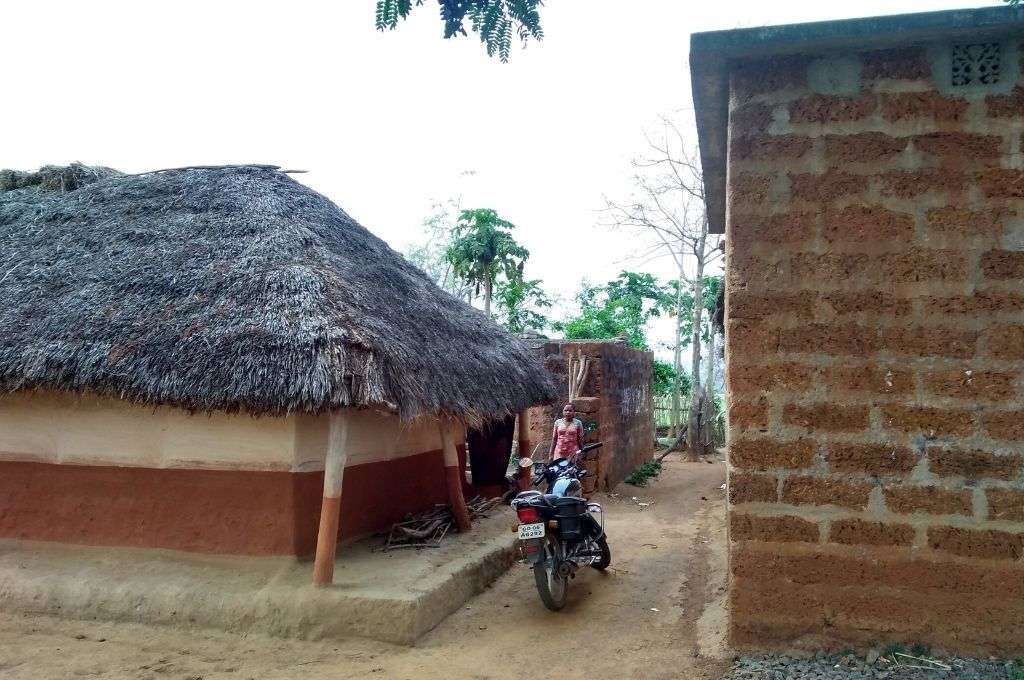 दो घरों के बीच खड़ी एक मोटरसाइकल-प्रधान मंत्री ग्रामीण आवास योजना ओडिशा