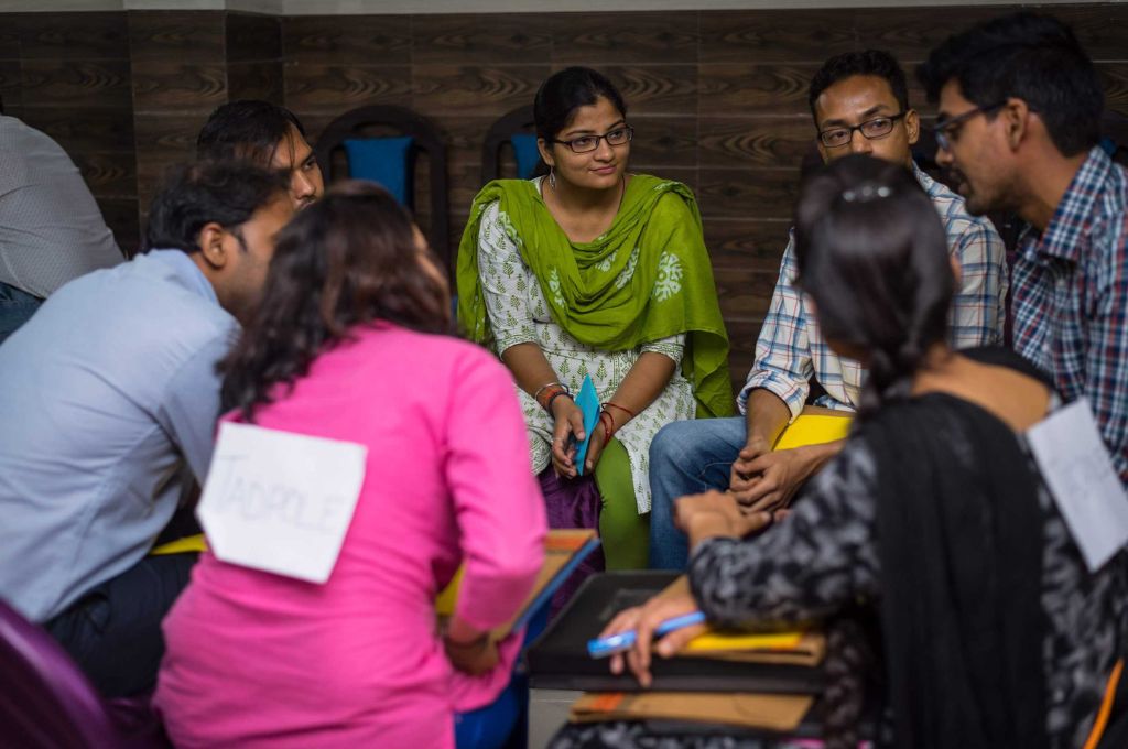 टेबल के चारों ओर बैठे युवा पेशेवरों से बात करती महिला_कौशल विकास