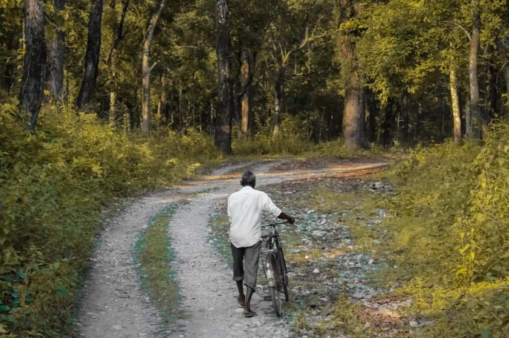 साइकिल को पकड़े हुए पगडंडी पर चलता हुआ एक आदमी_वन अधिकार