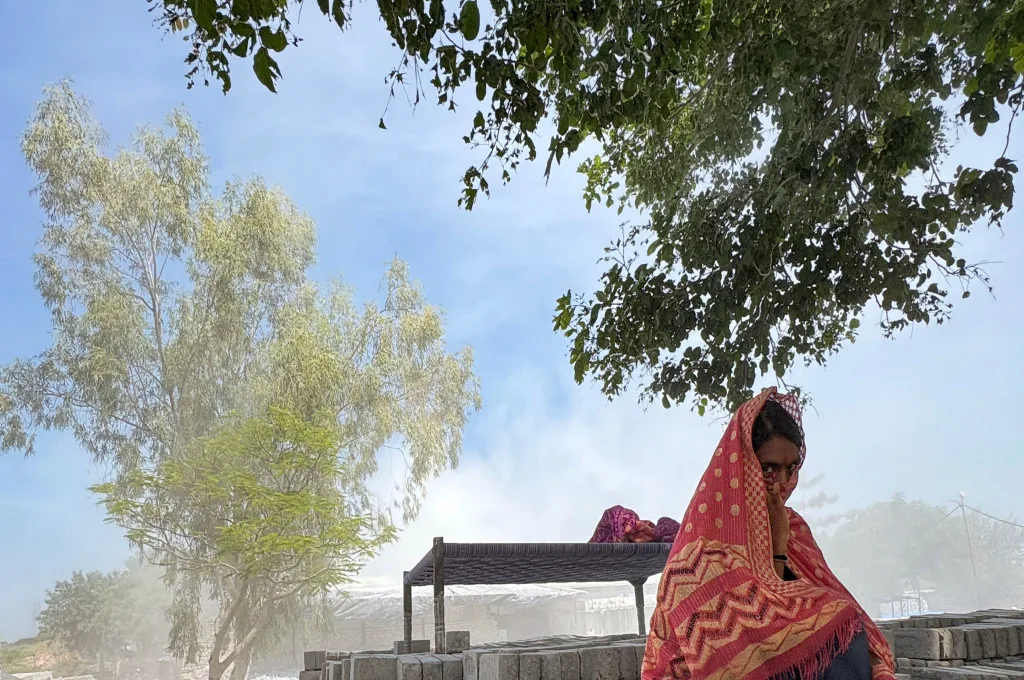 एक महिला श्रमिक ईंटों से उठती धूल के चलते मुंह ढके हुए है_फ्लाई ऐश ईंट कारखानें