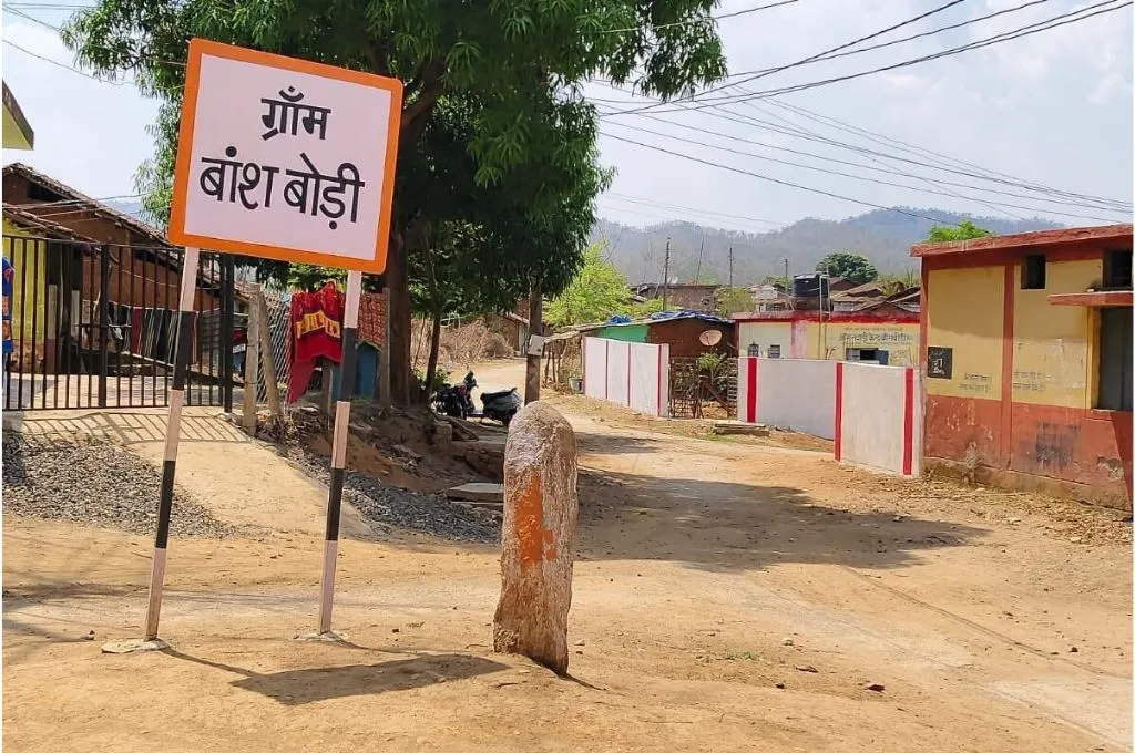 एक गांव के साइन बोर्ड के पास खड़ी ग्रामीण महिला_वन ग्राम